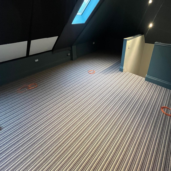 A room with sloped ceilings and a skylight features striped carpeting and scattered orange circles on the floor.