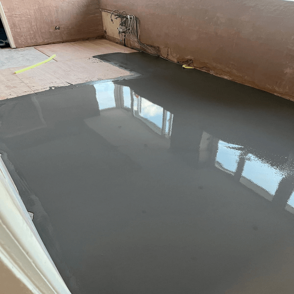 Commercial Flooring. A room with freshly applied, smooth, gray self-leveling floor compound. Wall cables are visible, and a window reflection is on the floor. C